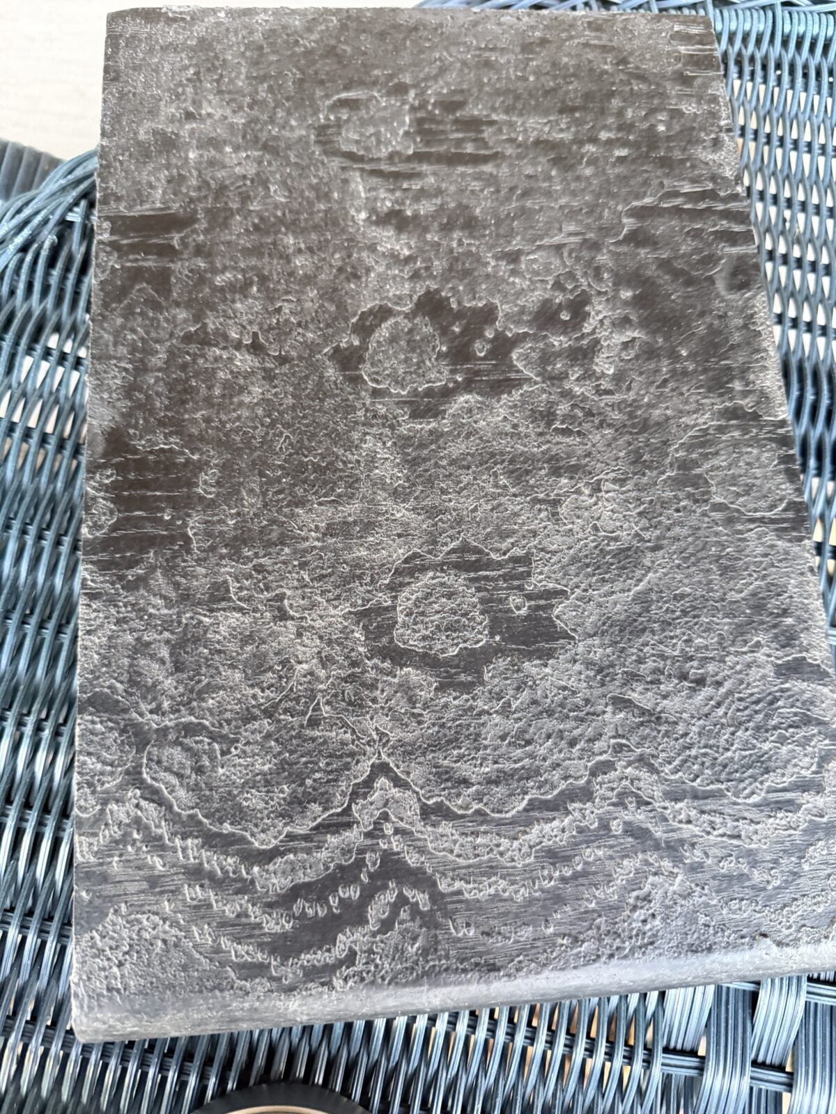 A close-up of a textured, gray stone slab with natural, wavy patterns and markings, resting on a blue woven surface.