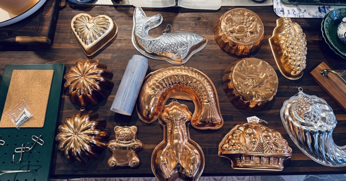A collection of vintage copper and silver gelatin molds—heart, fish, bear, grapes, lobster, basket, and flowers—arranged on a dark wooden table, perfect for adding charm to your spring home tour.