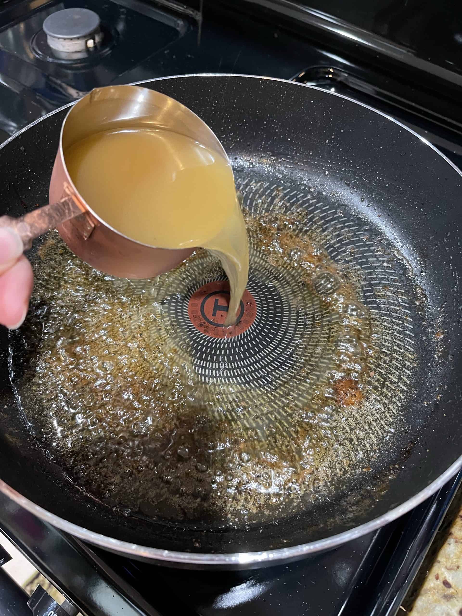 Pouring chicken broth into skillet