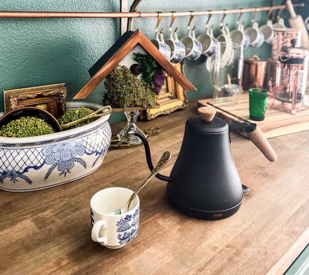 Black tea kettle with blue and white teacup and moss covered bird house