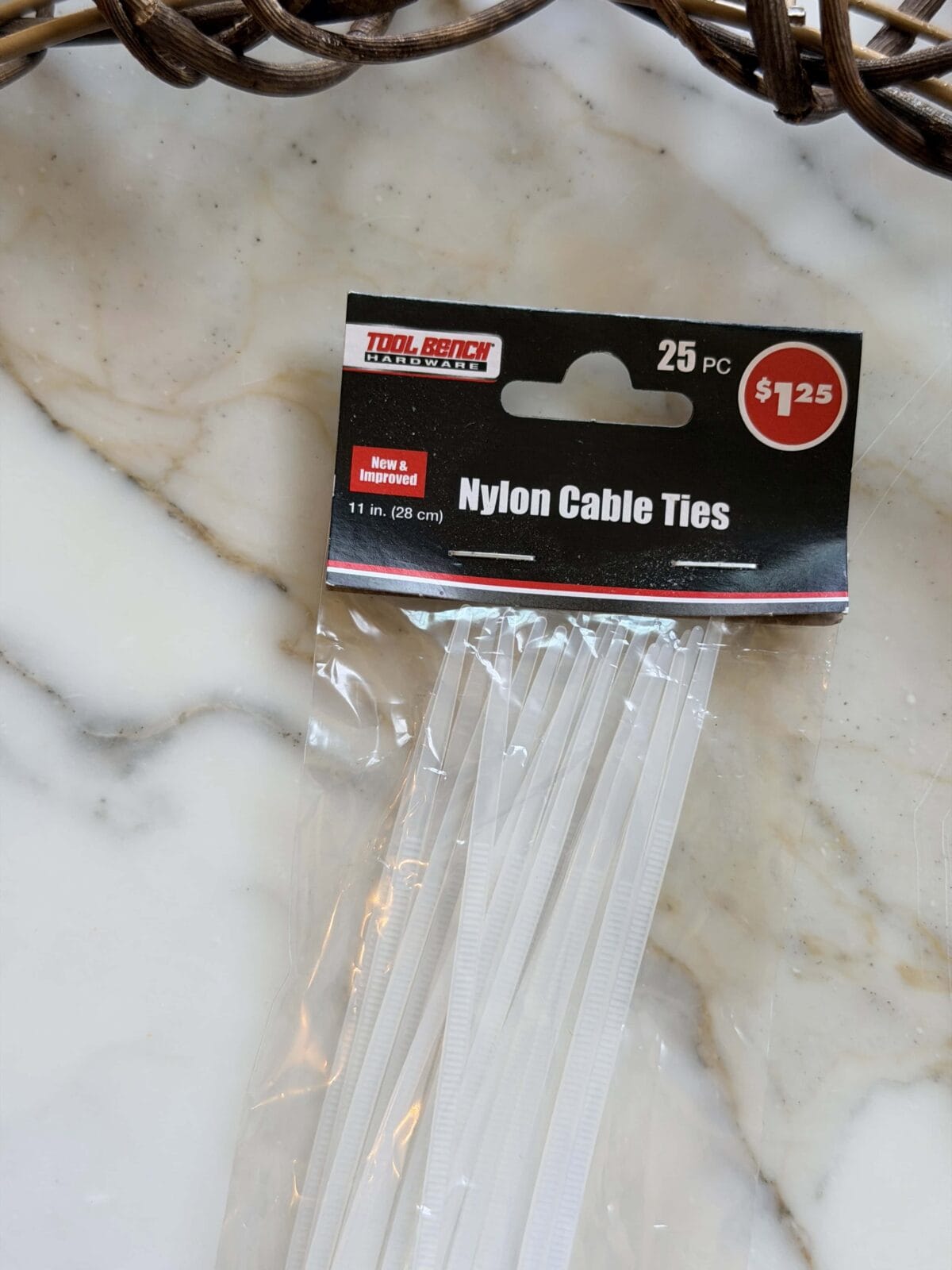 A pack of 25 white nylon cable ties in a clear plastic bag with a black and red label displaying the price of $1.25, placed on a marble surface.